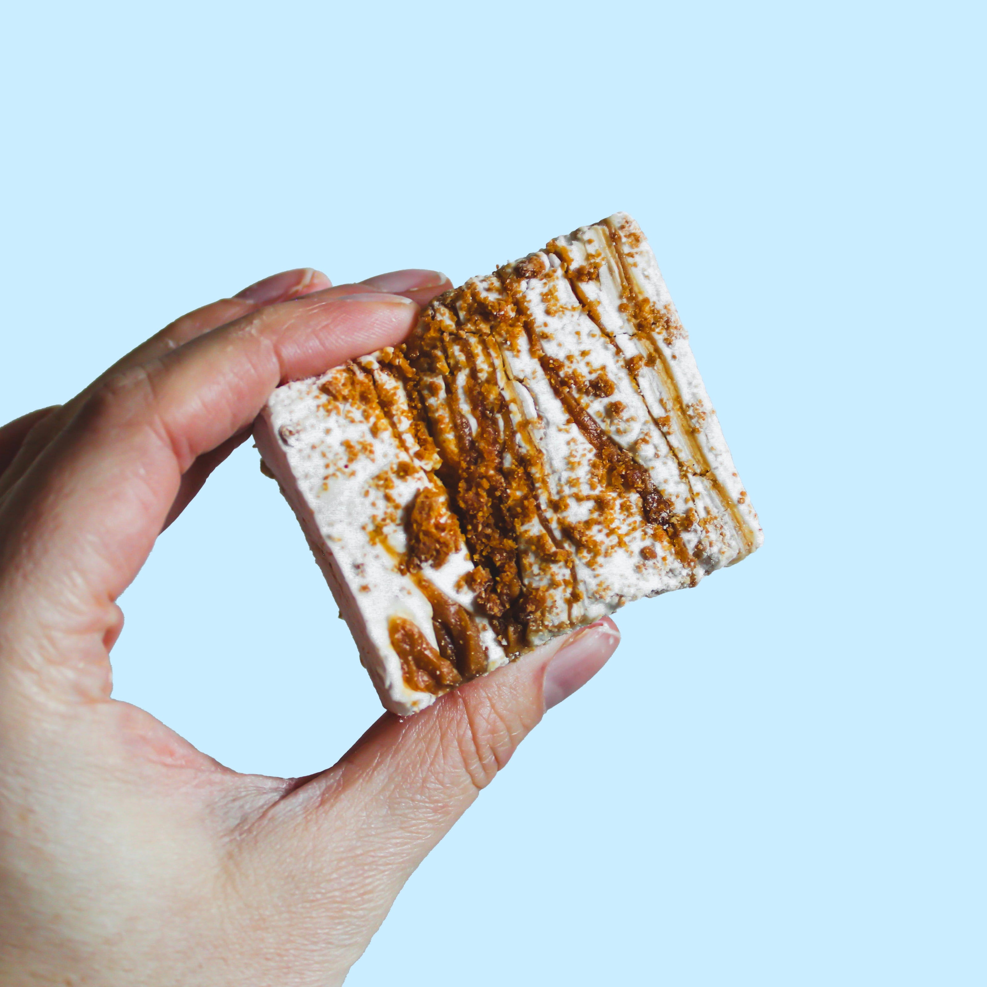 Hand holding a square of gourmet vanilla marshmallow made with Biscoff sauce and Biscoff biscuits.